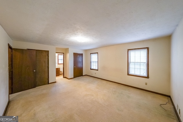 unfurnished bedroom featuring connected bathroom, light carpet, and a textured ceiling