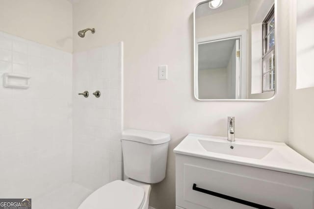 bathroom featuring toilet, tiled shower, and vanity