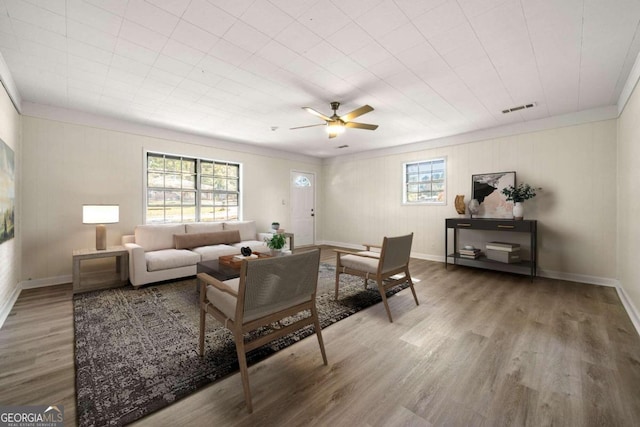 living room with wood-type flooring, ornamental molding, and ceiling fan