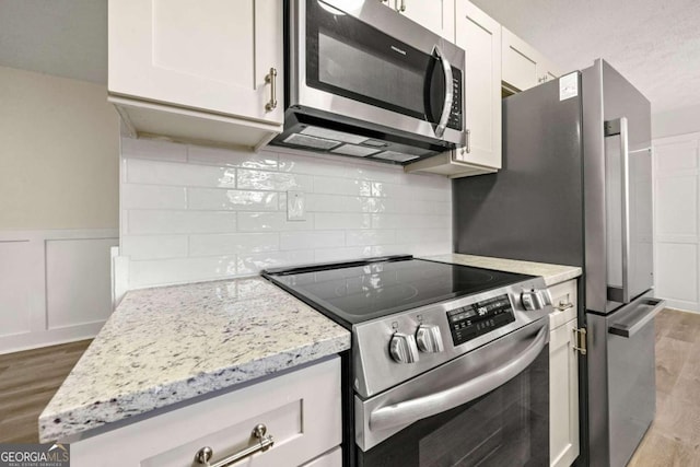 kitchen with appliances with stainless steel finishes, light hardwood / wood-style floors, light stone counters, decorative backsplash, and white cabinets