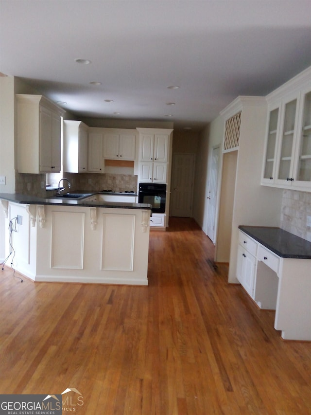 kitchen with tasteful backsplash, a breakfast bar, hardwood / wood-style flooring, white cabinets, and black oven