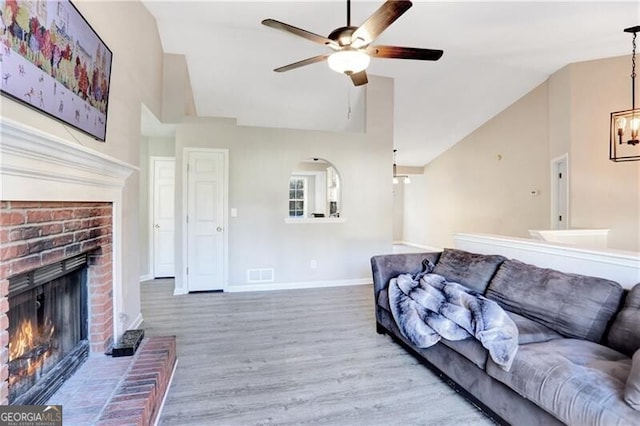 living room featuring a fireplace, ceiling fan with notable chandelier, lofted ceiling, and hardwood / wood-style flooring