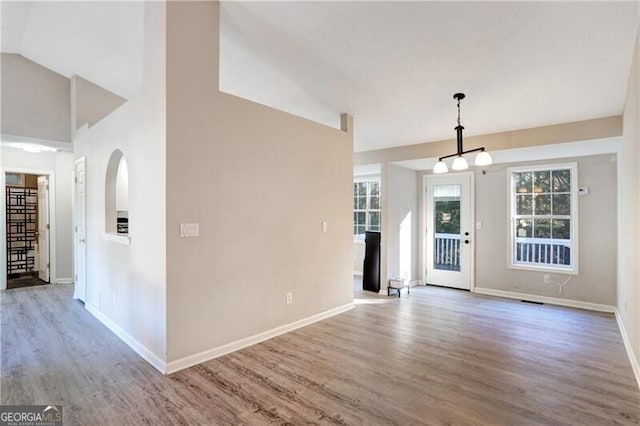 unfurnished living room with hardwood / wood-style floors, an inviting chandelier, and lofted ceiling