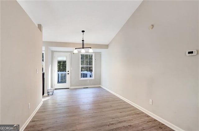 unfurnished dining area featuring a chandelier, lofted ceiling, and hardwood / wood-style flooring