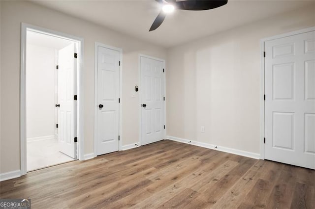 unfurnished bedroom featuring hardwood / wood-style floors, ensuite bath, ceiling fan, and multiple closets