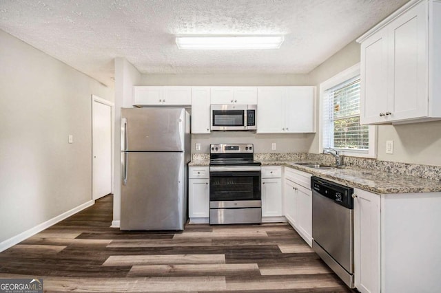 kitchen featuring sink, light stone countertops, appliances with stainless steel finishes, dark hardwood / wood-style flooring, and white cabinetry