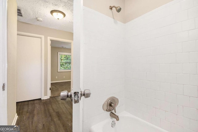 bathroom with a textured ceiling, bathtub / shower combination, and hardwood / wood-style flooring