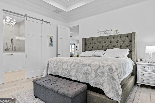 bedroom featuring an inviting chandelier, ensuite bath, wood-type flooring, crown molding, and a barn door