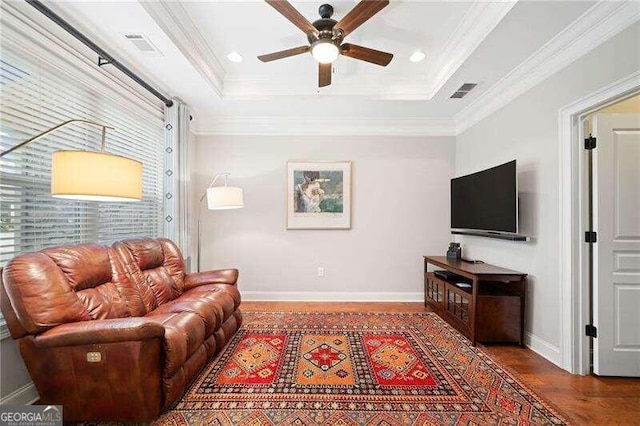 living room featuring wood-type flooring, a tray ceiling, ceiling fan, and crown molding