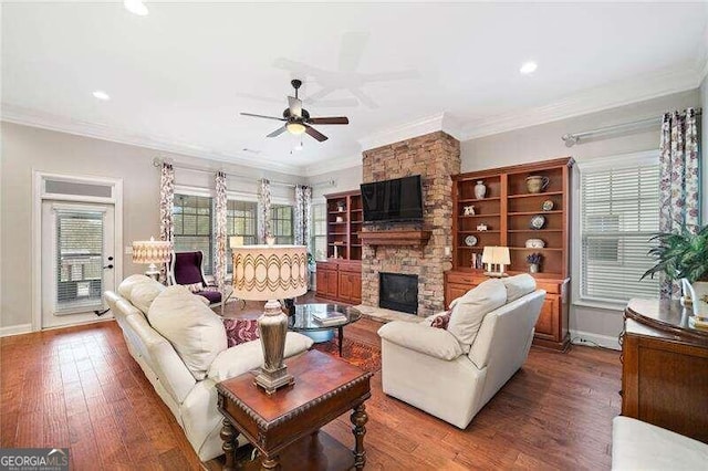 living room with wood-type flooring, a stone fireplace, ceiling fan, and ornamental molding