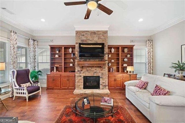 living room with a stone fireplace, ceiling fan, dark wood-type flooring, and ornamental molding