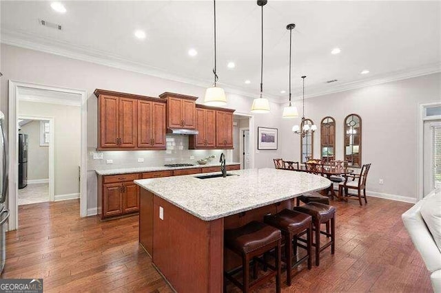 kitchen featuring light stone countertops, crown molding, sink, decorative light fixtures, and an island with sink