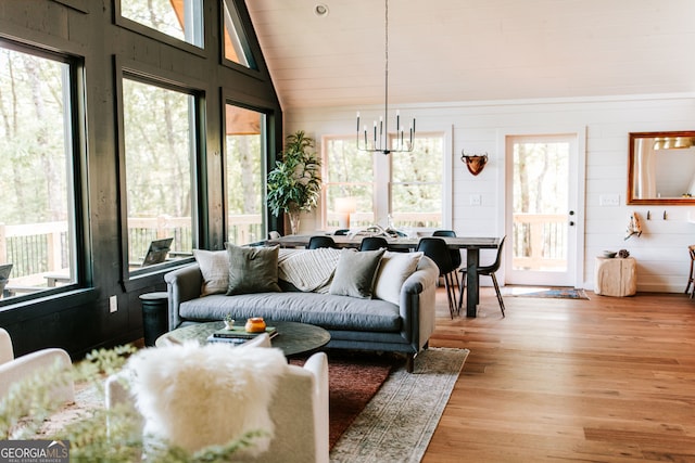 living room with a notable chandelier, light hardwood / wood-style floors, lofted ceiling, and a wealth of natural light