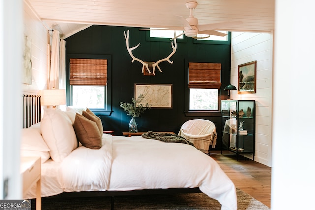 bedroom with ceiling fan, wooden walls, wood-type flooring, and lofted ceiling