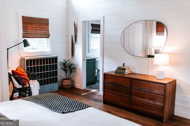 bedroom featuring ensuite bathroom, wooden walls, and dark wood-type flooring