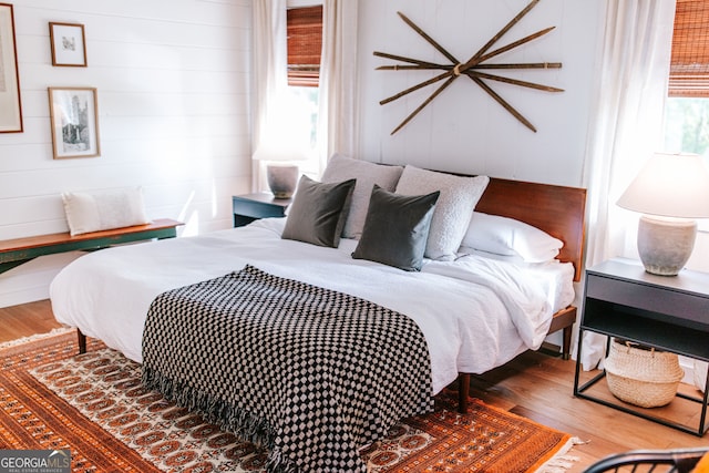 bedroom with hardwood / wood-style floors, wooden walls, and multiple windows