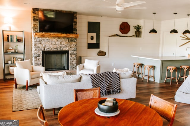 living room with hardwood / wood-style flooring, ceiling fan, a stone fireplace, and sink