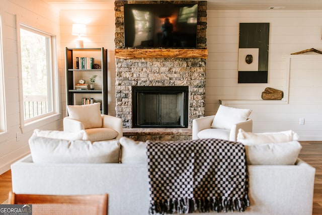 living room with wood-type flooring, a stone fireplace, a healthy amount of sunlight, and wood walls