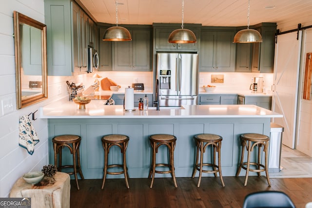 kitchen with appliances with stainless steel finishes, a kitchen breakfast bar, a barn door, decorative light fixtures, and dark hardwood / wood-style floors