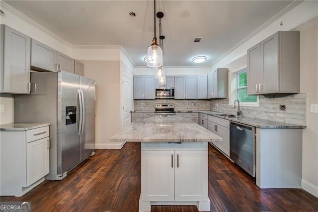 kitchen with appliances with stainless steel finishes, dark hardwood / wood-style flooring, sink, decorative light fixtures, and a center island