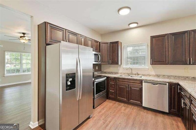 kitchen with light stone counters, dark brown cabinetry, stainless steel appliances, sink, and light hardwood / wood-style floors