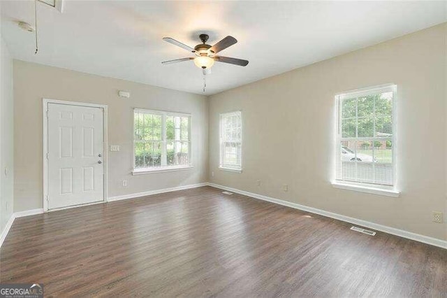 empty room featuring plenty of natural light, ceiling fan, and dark hardwood / wood-style flooring