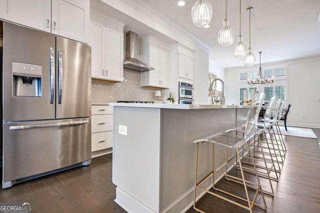 kitchen featuring a breakfast bar, a kitchen island with sink, wall chimney exhaust hood, appliances with stainless steel finishes, and white cabinetry