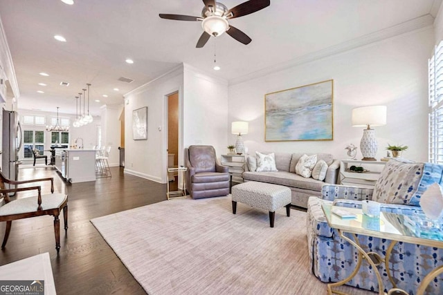 living room featuring ornamental molding, ceiling fan with notable chandelier, and dark wood-type flooring