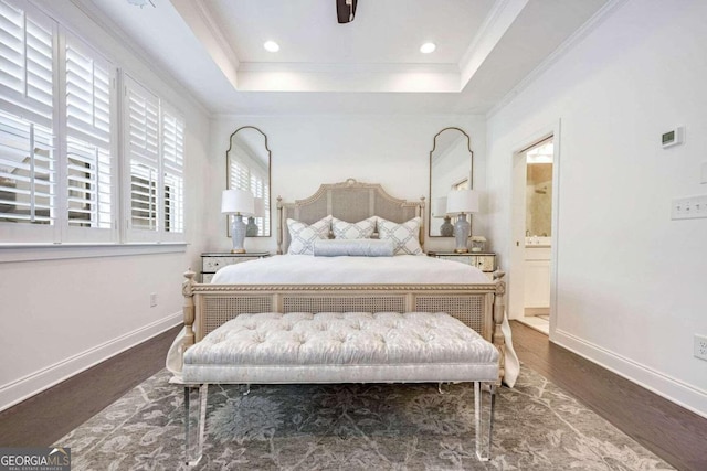 bedroom with dark hardwood / wood-style floors, ensuite bath, a tray ceiling, and ornamental molding