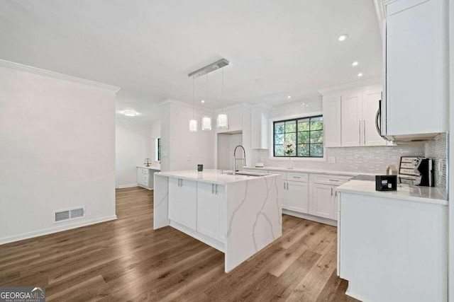 kitchen with white cabinetry, a center island with sink, hanging light fixtures, and light hardwood / wood-style floors