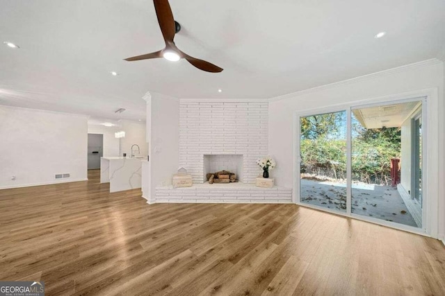 unfurnished living room featuring ceiling fan, sink, crown molding, a fireplace, and hardwood / wood-style flooring