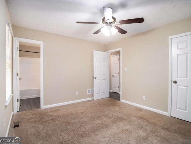 unfurnished bedroom featuring connected bathroom, ceiling fan, a textured ceiling, and dark colored carpet