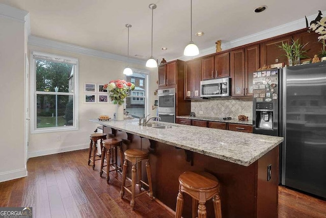 kitchen with dark wood-type flooring, ornamental molding, appliances with stainless steel finishes, decorative light fixtures, and light stone counters