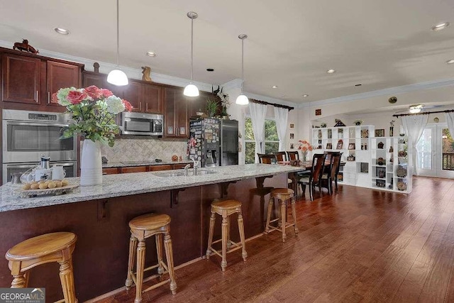 kitchen with crown molding, a breakfast bar area, dark hardwood / wood-style floors, decorative light fixtures, and stainless steel appliances