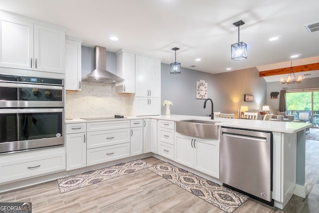 kitchen featuring appliances with stainless steel finishes, wall chimney exhaust hood, sink, pendant lighting, and light hardwood / wood-style flooring