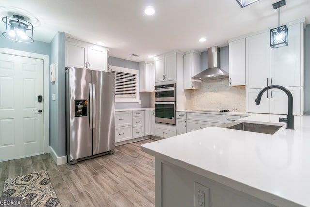 kitchen featuring white cabinets, decorative light fixtures, wall chimney range hood, and stainless steel appliances