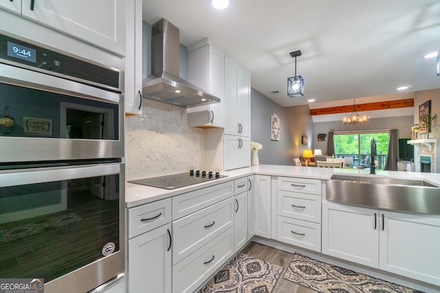 kitchen with stainless steel double oven, black electric cooktop, sink, wall chimney range hood, and white cabinets