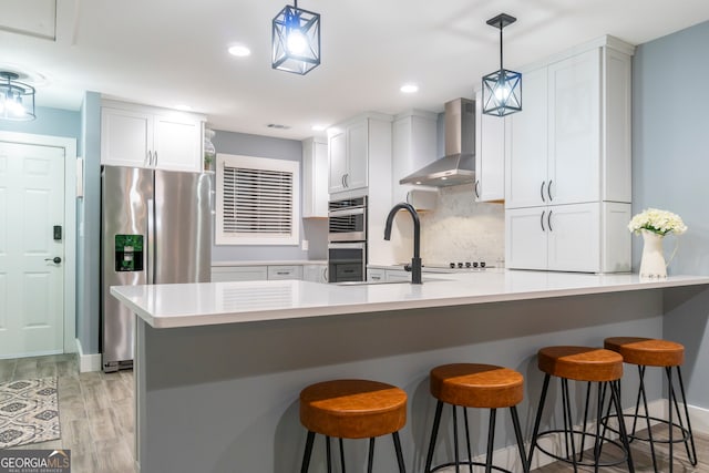 kitchen featuring a breakfast bar area, white cabinets, stainless steel appliances, and wall chimney range hood