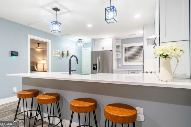 kitchen featuring hardwood / wood-style floors, white cabinets, sink, stainless steel refrigerator with ice dispenser, and decorative light fixtures