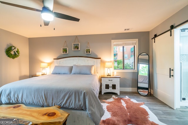 bedroom featuring hardwood / wood-style flooring, ceiling fan, and a barn door