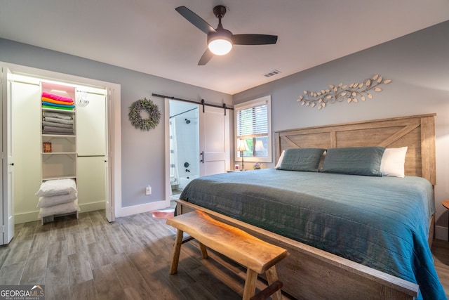 bedroom with ceiling fan, a barn door, and wood-type flooring