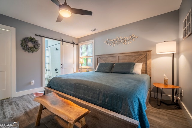 bedroom featuring a barn door, ceiling fan, ensuite bath, and wood-type flooring