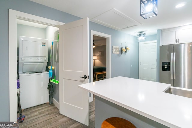 kitchen with light hardwood / wood-style floors, a breakfast bar, white cabinets, stainless steel fridge with ice dispenser, and stacked washer and dryer