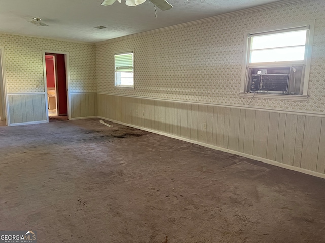 carpeted empty room featuring a textured ceiling, ceiling fan, crown molding, and wood walls