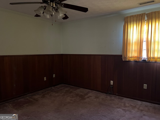 carpeted empty room featuring a textured ceiling, ceiling fan, ornamental molding, and wood walls