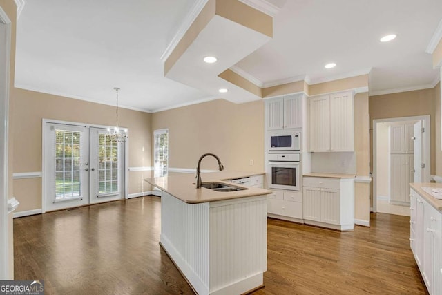 kitchen with white appliances, a kitchen island with sink, dark wood-type flooring, sink, and pendant lighting