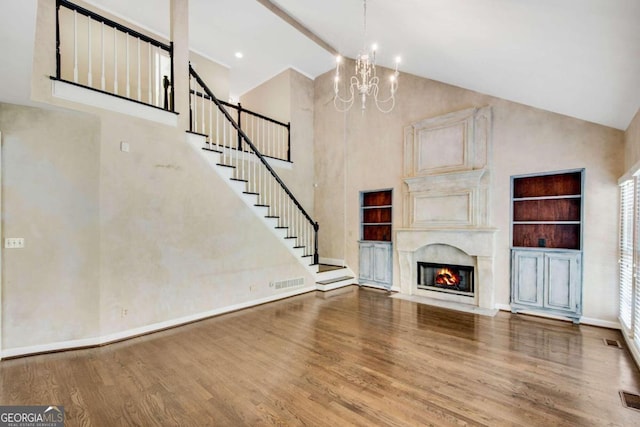 unfurnished living room featuring a high end fireplace, built in shelves, wood-type flooring, an inviting chandelier, and high vaulted ceiling