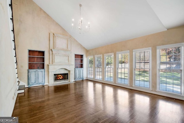 unfurnished living room with dark hardwood / wood-style flooring, high vaulted ceiling, built in features, and a notable chandelier