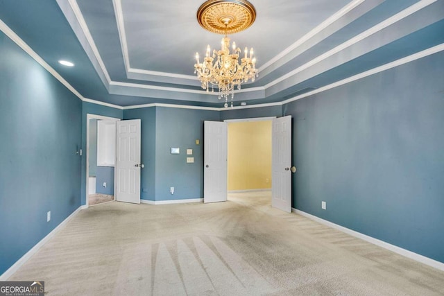 carpeted empty room featuring a raised ceiling, crown molding, and a notable chandelier