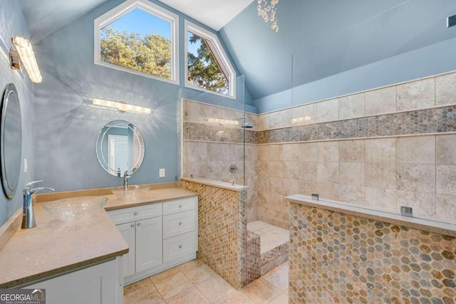 bathroom with vanity, lofted ceiling, tile patterned flooring, tiled shower, and tile walls